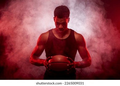 Basketball player side lit with red color holding a ball against smoke background. Serious concentrated african american man. - Powered by Shutterstock