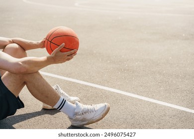 A basketball player sitting on the court, holding a basketball, reflecting quietly in the sun.

 - Powered by Shutterstock