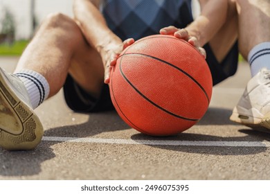 A basketball player sitting on an outdoor court, holding an orange ball between their legs.

 - Powered by Shutterstock