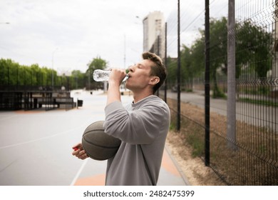 basketball player takes a break from playing on an outdoor court to drink water from a plastic bottle - Powered by Shutterstock