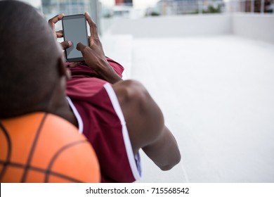 Basketball player using mobile phone while relaxing on terrace - Powered by Shutterstock