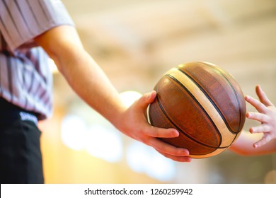 Basketball Referee Giving A Basketball To A Young Player At A Game In An Old School Sports Gym. Selective Focus On The Ball.