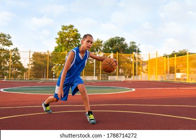 Basketball. A teenage boy in blue sportswear plays a basketball. In the background is a sports field. Concept of sports games
