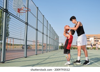 Basketball trainer showing how to shoot basketball to a child with a leg prosthesis. Coach training a kid.