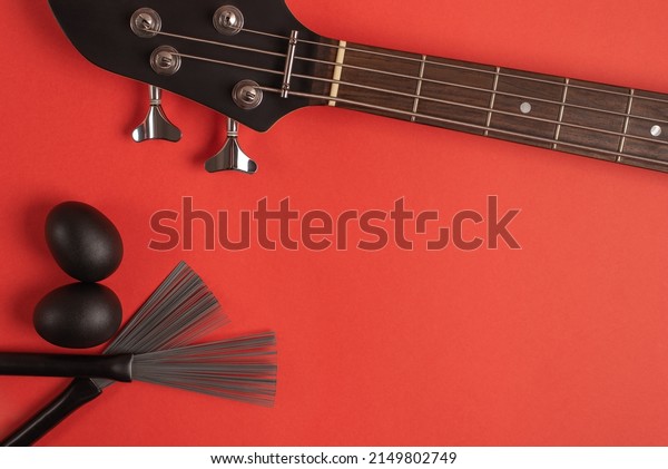 Bass guitar neck,\
shakers and drum brushes on a bright red background. Top view, flat\
lay, space for text. 