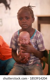 Basse, Gambia, Africa, January 30, 2020: Vertical Photo - Portrait Of Young Mandinka Girl With Braids, Sitting On Chair, Looking Into Camera Posing In Front Of Other Students Inside A School Classroom