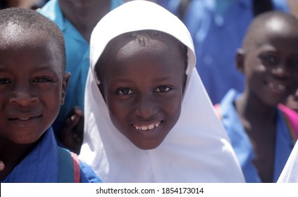 Basse, Gambia, Africa, January 30, 2020: Horizontal Photo - Portrait Of Young Mandinka Girl With White Head Cover,  Looking Into Camera, Posing Between Other Students Outdoors On A Sunny Day