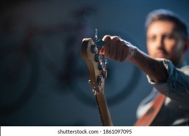 the bassist adjusts the electric bass guitar, in the foreground of the pegs and fretboard, close-up