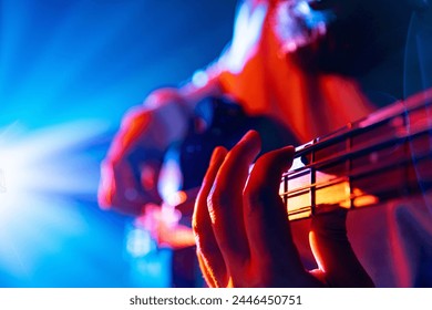 Bassist's hands playing melodic chords of new track in action with colorful concert light flare in background. Concept of rock and classic music, hobby and work, energy, music festivals, concerts. Ad