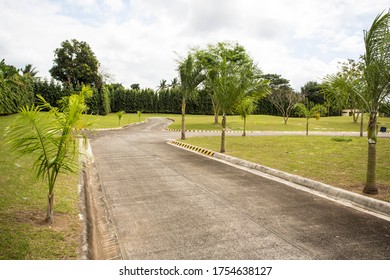 Batangas, Philippines; February 2019 - A Concrete Road With Luscious Plants And Trees And Green Lawn  