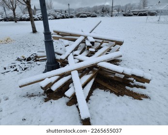 A batch of boards left sitting on a field with snow covering them.