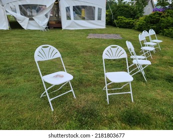 A Batch Of White Lawn Chairs Left Sitting Out Randomly In A Park.