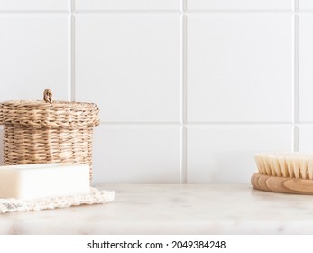 Bath background front view with straw box, wood brush for body and white soap on white marble shelf and wall tiles. Front view. Copy space