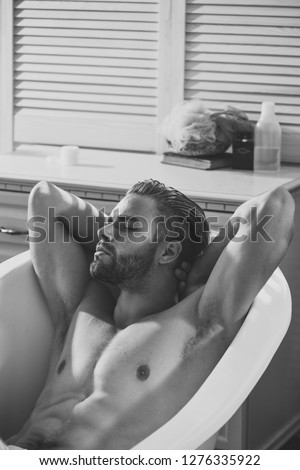 Bath, bathing, shower, spa. Man with muscular torso, abs, arms, biceps, triceps in bath. Hygiene, grooming, health. Bodycare, wellness, pleasure, relax. Sexy macho relax naked in bathtub in bathroom.