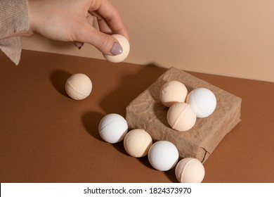 Bath Bombs With Paper Gift Box On Beige Background. The Girl's Hand With Organic Spa Bomb.