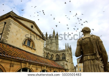 Bath (England, UK) Stone statue of the roman in Antique Roman Baths complex, flying birds in sky and Abbey Cathedral at background. City of Bath is a UNESCO World Heritage Site. 