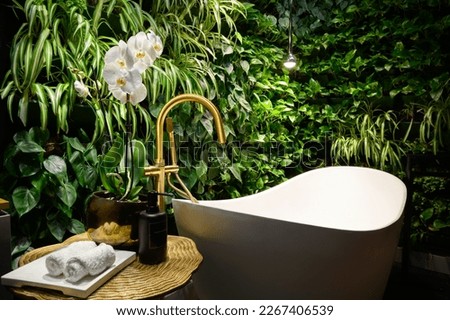 Bath in modern beauty salon, luxury bathroom interior in spa with vertical garden. Green plants wall, flowers and bathtub in hotel. Concept of nature, landscaping, water, wellness, room.