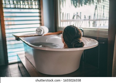 Bath taking woman relaxing in bathtub of hotel room at luxury overwater bungalow resort in Bora Bora, Tahiti.