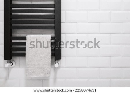 bath towel hanging on modern metal radiator on ceramic brick tile background in restroom in apartment with contemporary interior, luxury towel dryer indoors
