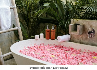 Bath Tub With Flower Petals, Towel And Beauty Products. Organic Spa Relaxation In Luxury Bali Outdoor Bathroom.