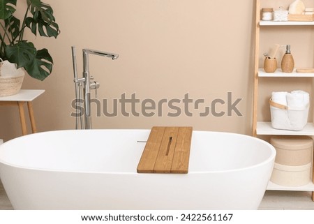 Bath tub with wooden board and different personal care products and accessories on shelving unit in bathroom