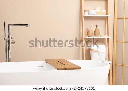 Bath tub with wooden board and different personal care products and accessories on shelving unit in bathroom