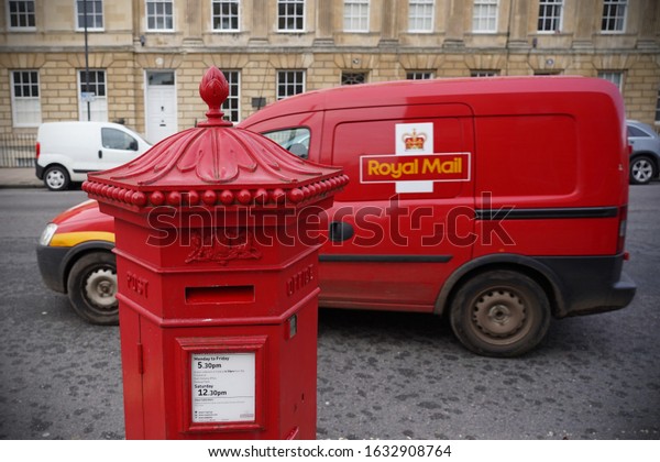 Bath, UK - November 30, 2019: A traditional\
British red post box and Royal Mail post delivery van are seen on a\
city centre street.