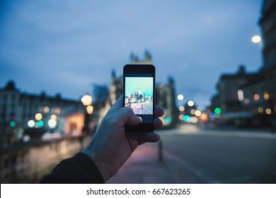 BATH, UNITED KINGDOM - MAR 7, 2017:Personal Perspective Pov Of Man Taking Photograph With The Mobile Phone Smartphone Of The Illuminated Cathedral Bath Abbey In Bath, United Kingdom 