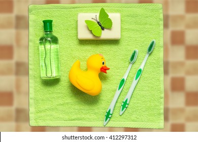 Bathroom Accessories On A Green Towel. Rubber Ducky, Toothbrushes, Soap And Lotion. Baby Care Accessories For Bath. Yellow Duckling Toy For Kids.