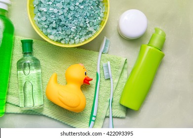 Bathroom Accessories On A Green Towel. Rubber Ducky, Toothbrushes, Soap And Lotion. Baby Care Accessories For Bath. Yellow Duckling Toy For Kids.