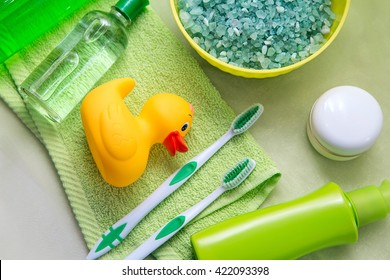 Bathroom Accessories On A Green Towel. Rubber Ducky, Toothbrushes, Soap And Lotion. Baby Care Accessories For Bath. Yellow Duckling Toy For Kids.