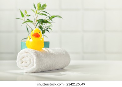 Bathroom accessories on white bathroom countertop against tile wall - white towel, rubber duckling and house plant, copy space