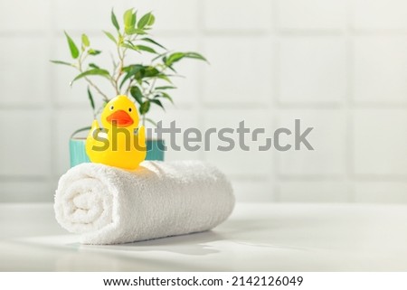 Bathroom accessories on white bathroom countertop against tile wall - white towel, rubber duckling and house plant, copy space