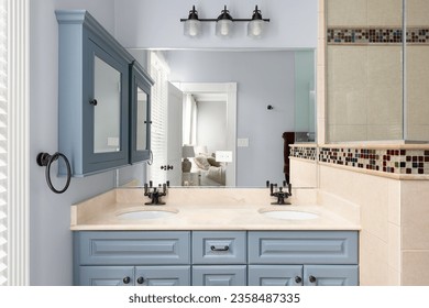 A bathroom with blue cabinet and medicine cabinet, a marble countertop, tiled shower, and view towards the primary bedroom. - Shutterstock ID 2358487335