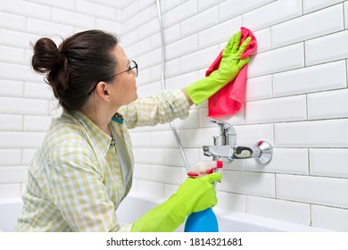 Bathroom cleaning, housewife washing white tile wall with detergent and rag, copy space. Hygiene, purity, cleanliness concept