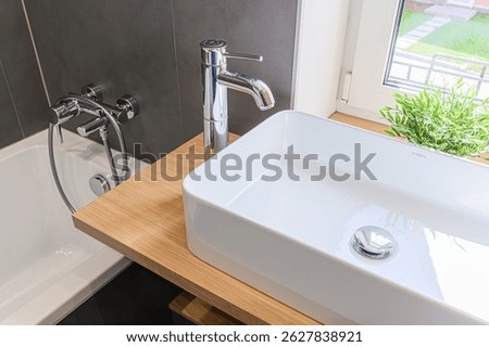 Bathroom close-up: White rectangular sink with chrome faucet on a wooden countertop, next to a bathtub and window with greenery