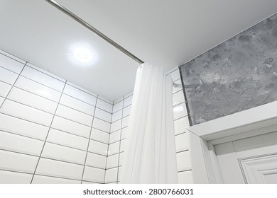 bathroom corner features white rectangular tiles with dark grout, a grey textured accent wall, a white shower curtain on a concealed ceiling rail, and a recessed ceiling light.
