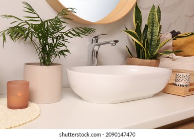 Bathroom counter with sink, candles and beautiful green houseplants near white marble wall