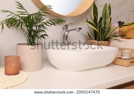 Bathroom counter with sink, candles and beautiful green houseplants near white marble wall