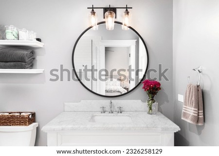 A bathroom detail with a white cabinet, black circular mirror, and light fixture, and a view to the bedroom.