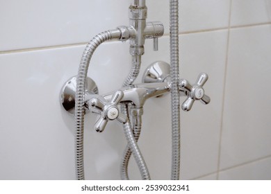 bathroom fixture, specifically shower or bathtub faucet with two handles. The handles are labeled with 'H' for hot water and 'C' for cold water. The fixture is made of shiny chrome material and water - Powered by Shutterstock