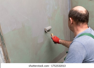 In The Bathroom, A General Construction Worker Applies Moisture Insulation Using A Roller.