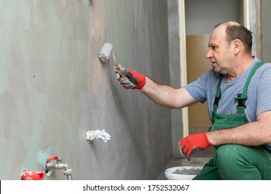 In The Bathroom, A General Construction Worker Applies Moisture Insulation Using A Roller.