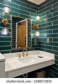 A Bathroom With Green Subway Tile Walls, Gold Lights, Marble Sink And A Gold Faucet.