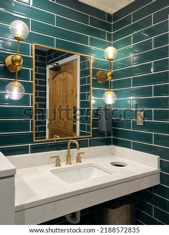 A bathroom with green subway tile walls, gold lights, marble sink and a gold faucet.