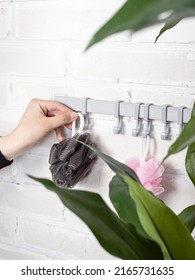 Bathroom hooks on white wall background. Plastic hanger with many hooks for towels, washcloths in bathroom. Woman takes a washcloth - Shutterstock ID 2165731635