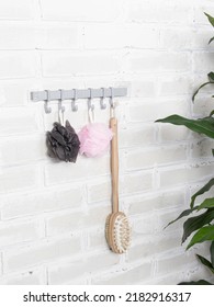 Bathroom hooks and plants on white wall background. Plastic hanger with many hooks for towels, washcloths in bathroom. Two washcloths and wooden brush for body - Shutterstock ID 2182916317