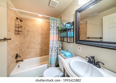 Bathroom Interior With Antique Fixtures And Ceramic Tile Walls. There Is A Vanity Sink With Ogee Edge Counter Beside Toilet With Storage Box On Top Near The Bathtub With Shower Curtain And Caddy.