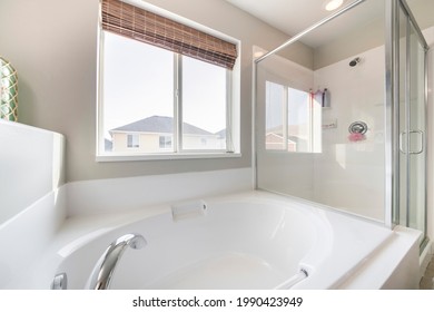 Bathroom Interior With Bathtub, Shower Stall And Window. On The Left There Is A Tub Against The Window With Native Roll Wooden Blinds Beside The Glass Enclosure With Aluminum Frames Of A Shower.