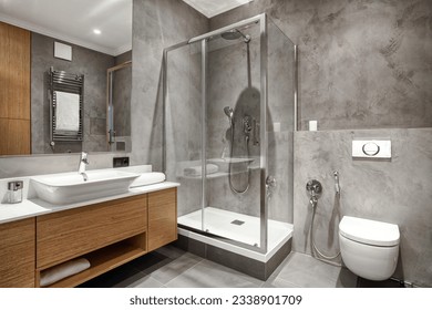 bathroom with luxury interior, glass shower cabin, wc bowl with concealed cistern tank, ceramic washbasin with faucet and wooden under sink cupboard with clean towel